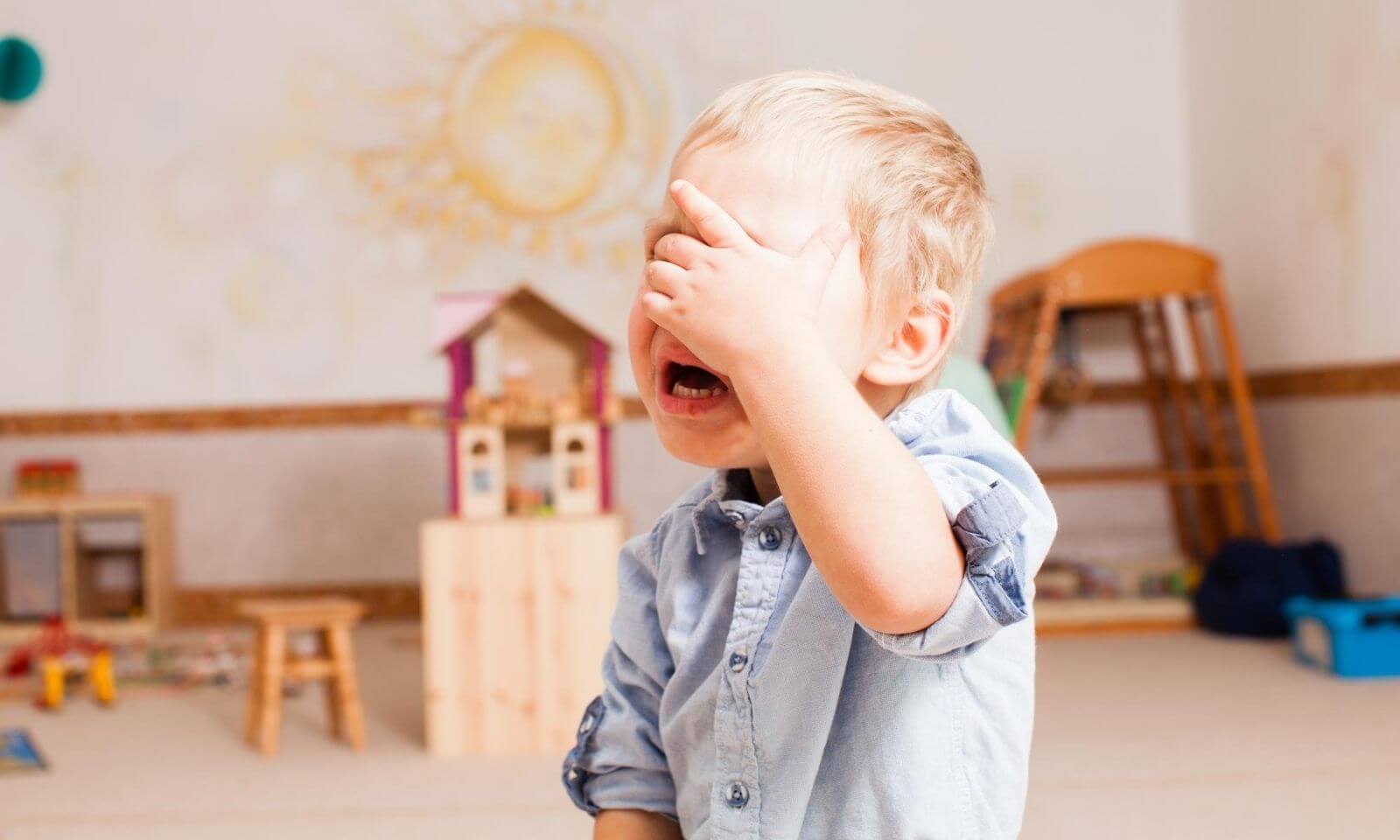 Bunt dwulatka – płaczący 2-latek, w tle pokój dziecięcy pełny zabawek