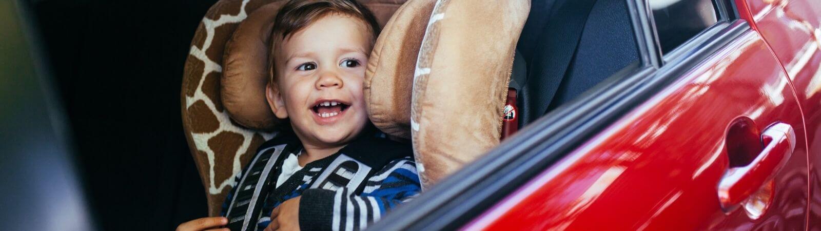 Jaki fotelik wybrać – uśmiechnięte dziecko siedzi w samochodzie w foteliku