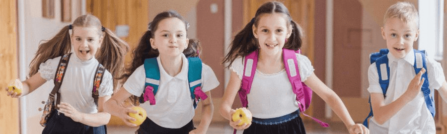 Uśmiechnięte dzieci z plecakami na plecach biegną szkolnym korytarzem